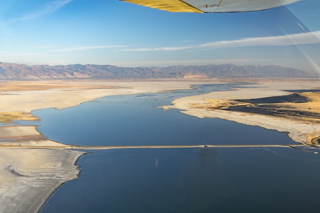 Aerial view looking Southeast (upstream) where the Jordan River flows under the Antelope Island Causeway from Farmington Bay (middle third of frame) into Great Salt Lake (bottom of frame).  Salt Lake City is visible at the base of the Wasatch Mountains (upper third, right side).  Farmington Bay used to be part of the lake, but now the bay is largely dry except for the Jordan River flowing through it.  Thanks to pilot Gabe Bowen and Friends of Great Salt Lake for the flight over Great Salt Lake.