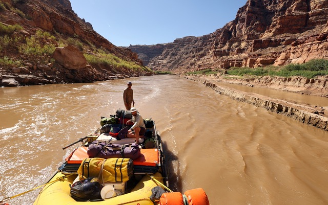 Peter Lefebvre, Returning Rapids researcher and OARS river guide, and Travis Custer, Returning Rapids member, motor by a plateau of mud in the Colorado River by Mille Crag Bend, below Cataract Canyon, on Sunday, Sept. 22, 2024. The sediment filled in when this area was submerged under Lake Powell. After the lake receded, mud remains.