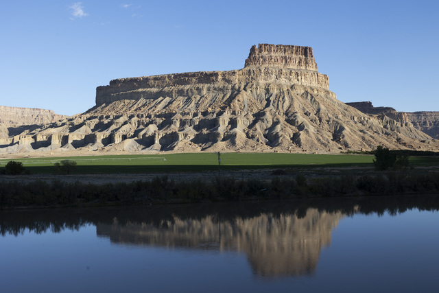 A arid mesa is reflected in the Green River, while green fields watered by the same river grow around the base of the mesa in Green River on Friday, Sept. 20, 2024. The Green River is vital for the melon growers and other farmers in Green River.