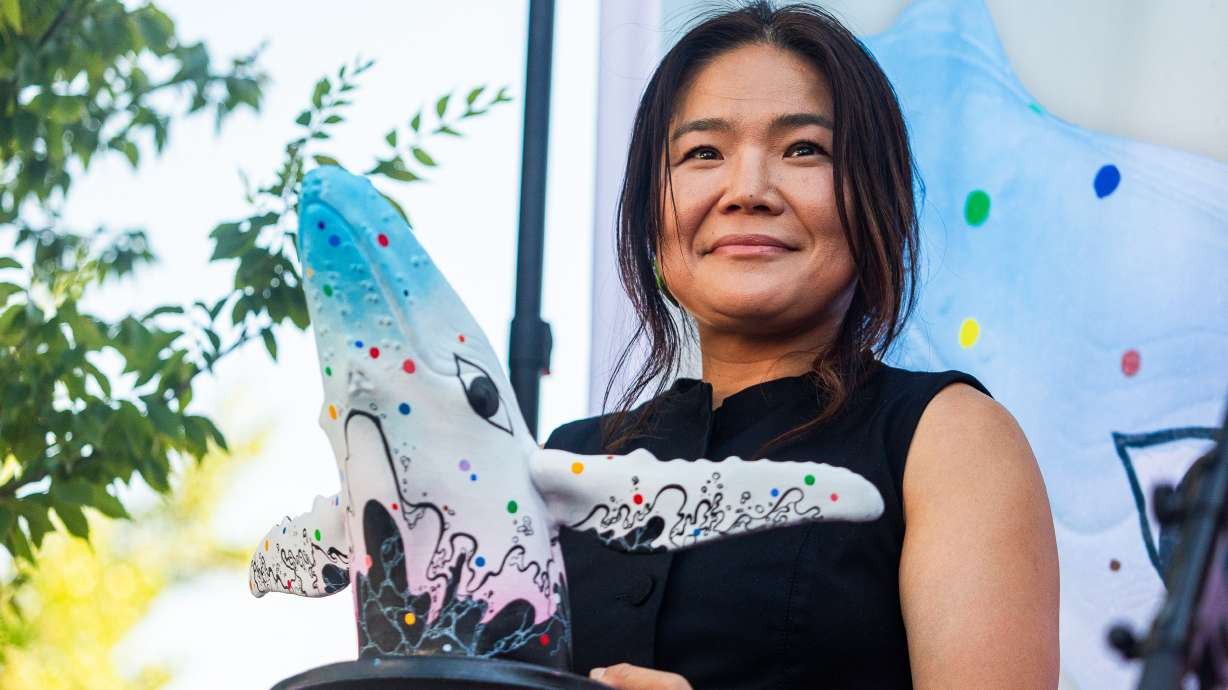 Salt Lake-based artist Jiyoun Lee-Lodge holds up a model of her mural "Open Your Eyes" during an unveiling of the new mural for "Out of the Blue" in Salt Lake City on Saturday. The mural will be painted on the city's whale sculpture in the coming weeks. (Carter Williams, KSL)