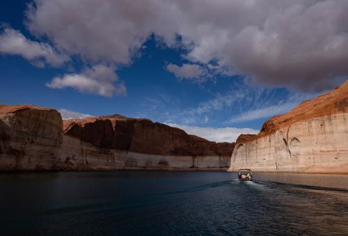 (Francisco Kjolseth | The Salt Lake Tribune) A Lake Powell rental pontoon boat motors down the main channel of the reservoir on Saturday, April 25, 2026, as bathtub rings are indicative of how far the waters levels have fallen since being at full capacity in the early 1980s.