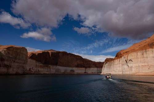 (Francisco Kjolseth | The Salt Lake Tribune) A Lake Powell rental pontoon boat motors down the main channel of the reservoir on Saturday, April 25, 2026, as bathtub rings are indicative of how far the waters levels have fallen since being at full capacity in the early 1980s.